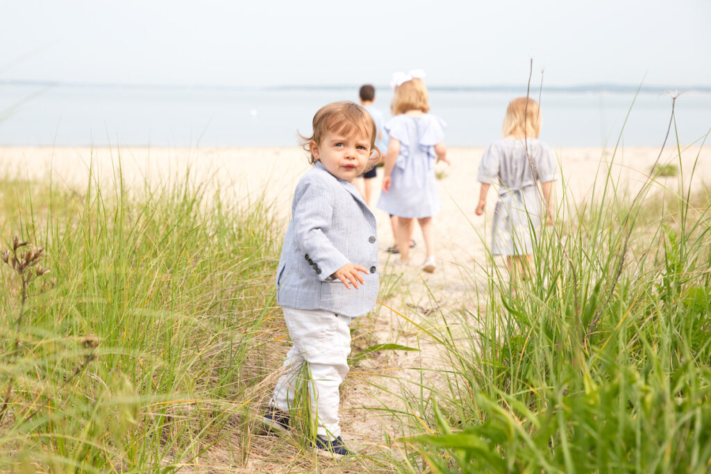 Children walk through the grasses on Long Beach in Sag Harbor, NY and little boy looks back towards the camera