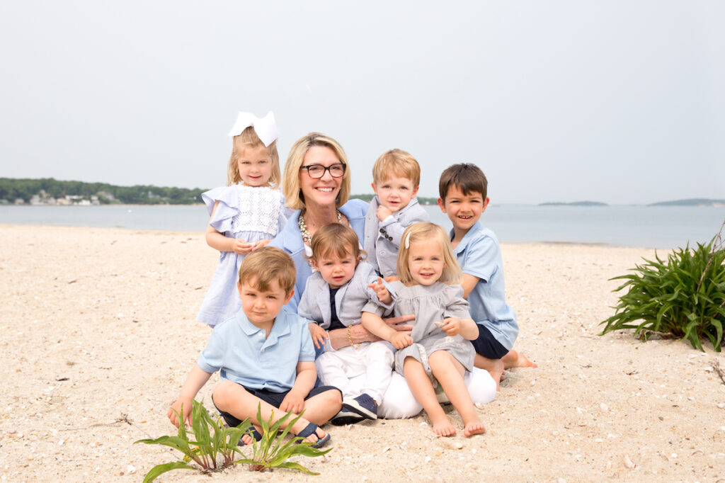 Grandmother sits on beach with her 6 grandchildren