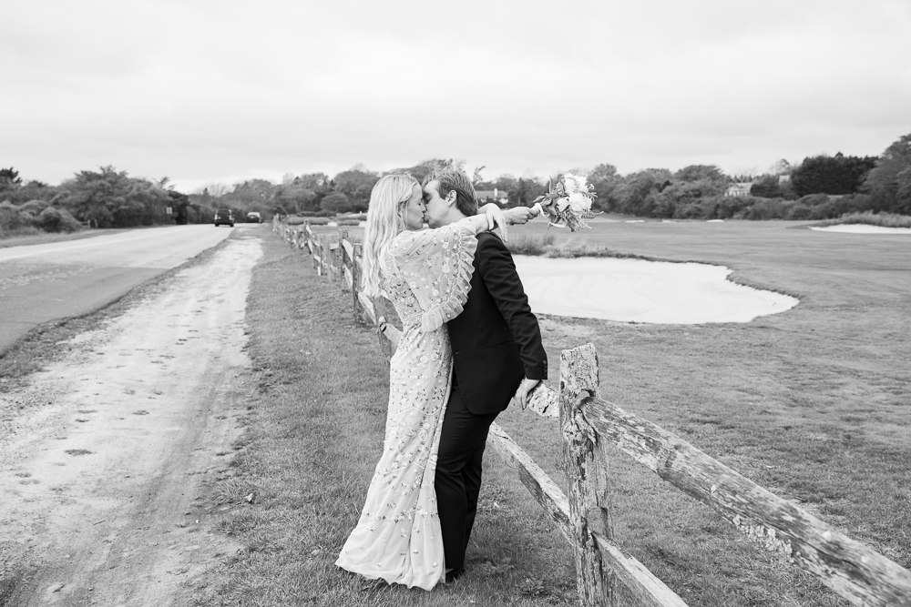 Newlywed couple kiss leaning against a fence in East Hampton, NY
