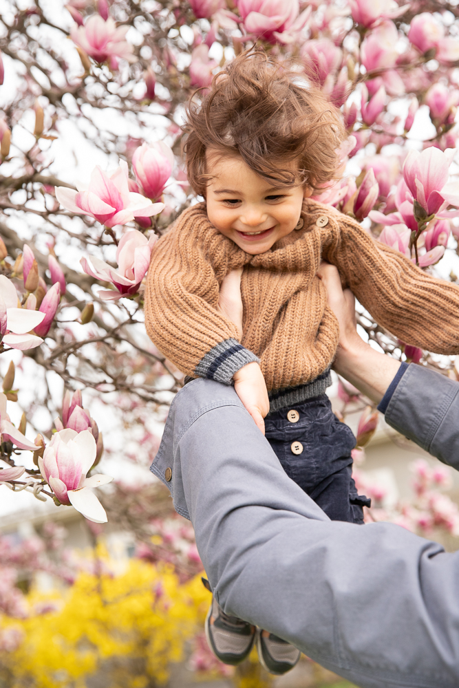 Baby boy lifted into the air with magnolias in the background