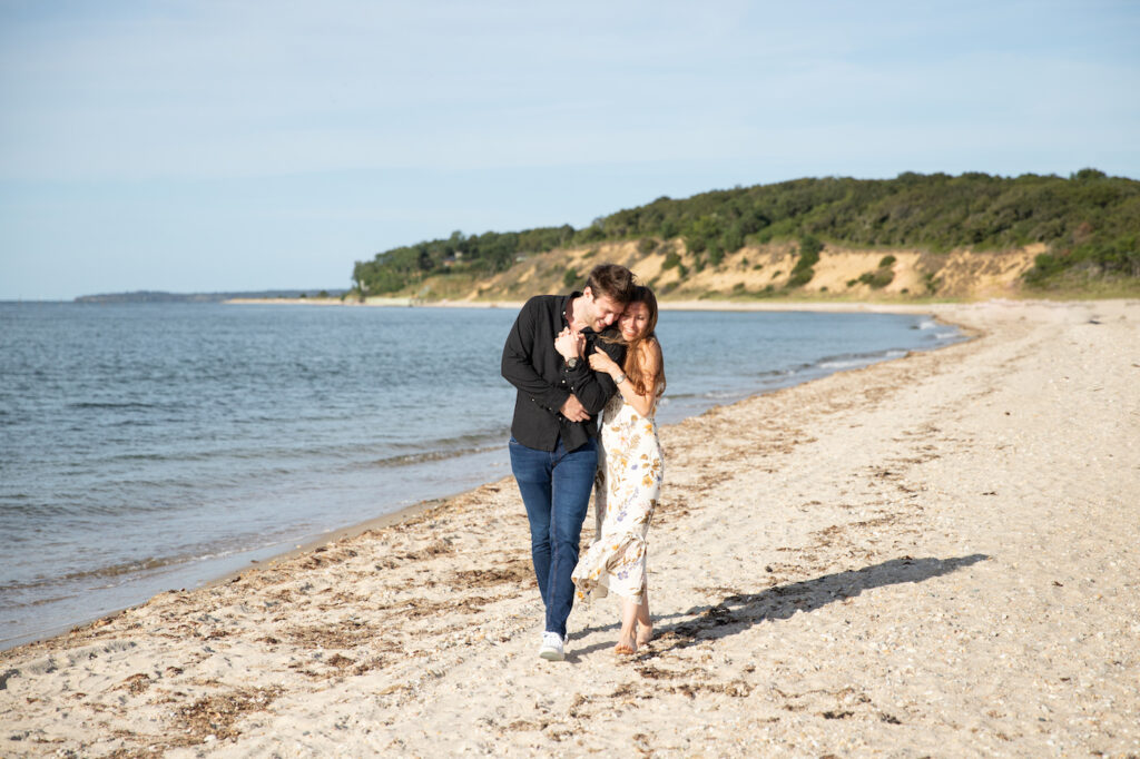 Newly engaged couple walk arm in arm along the shoreline at Maidstone Beach in Springs East Hampton