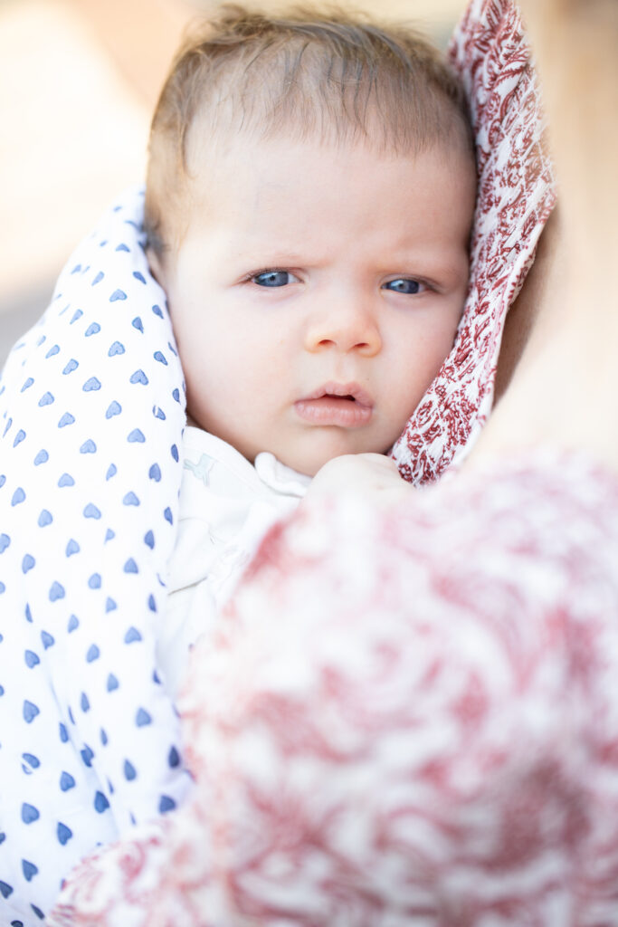 Newborn baby with blue eyes is snuggled up against mothers chest for a close up newborn photo of her face.