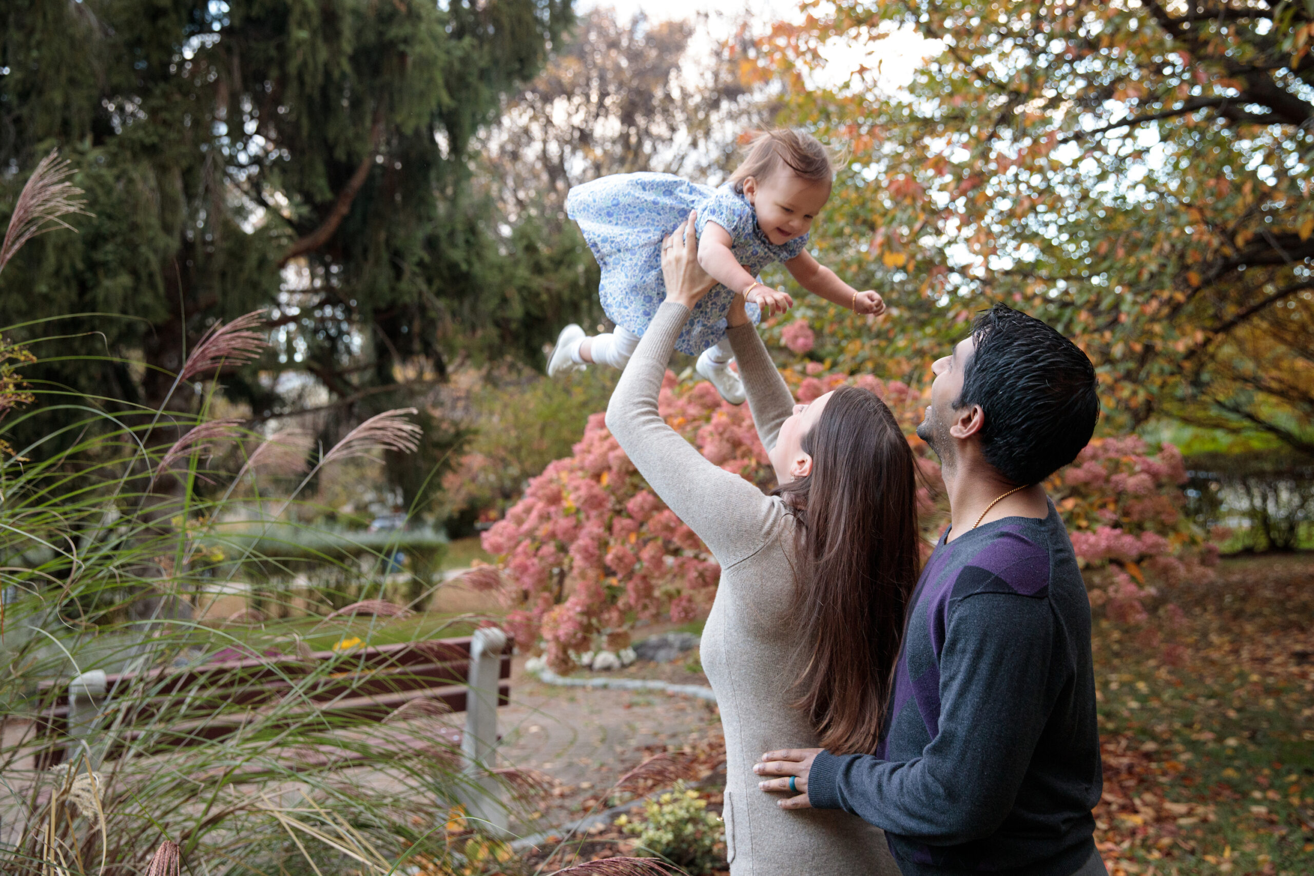 Mom holds baby in the air as dad looks on at Tot Park in Cold Spring, NY