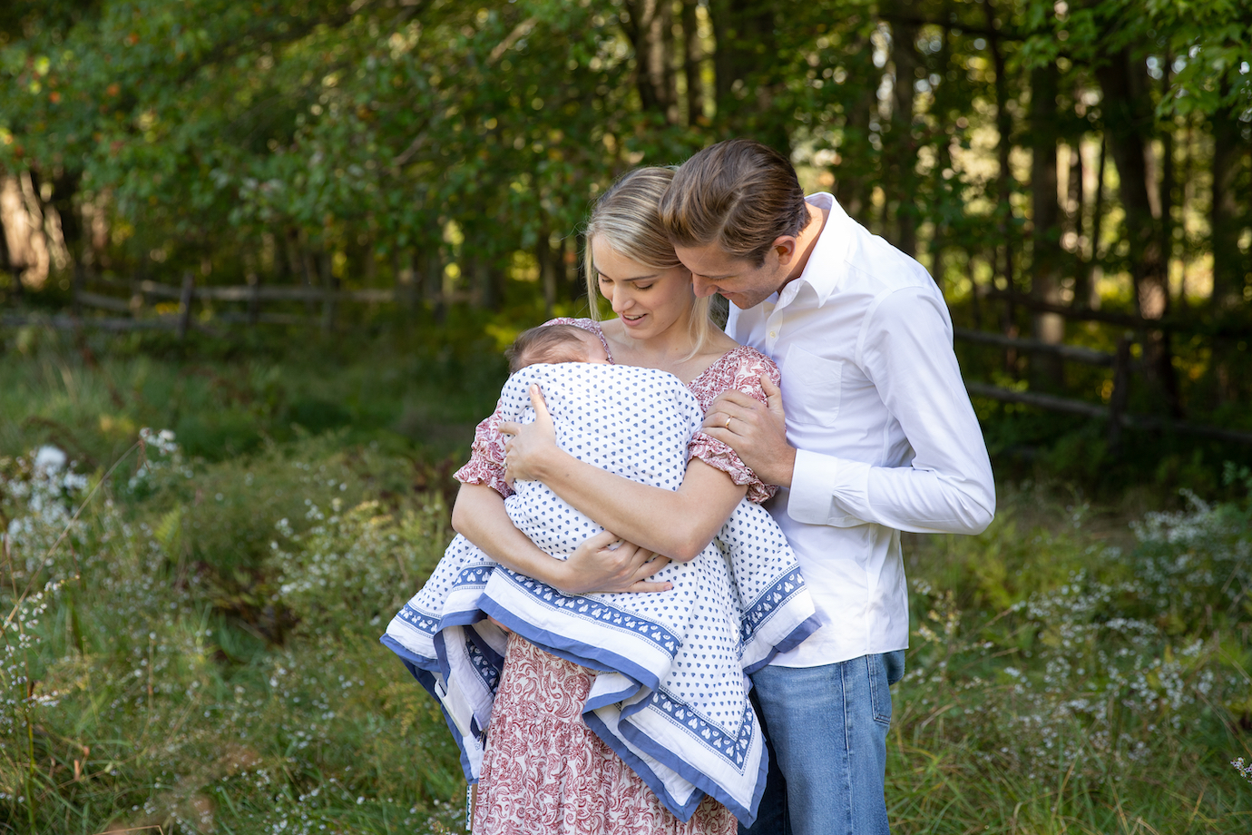 Couple hold their newborn while posing for newborn photo shoot in a field in Bedford, NY