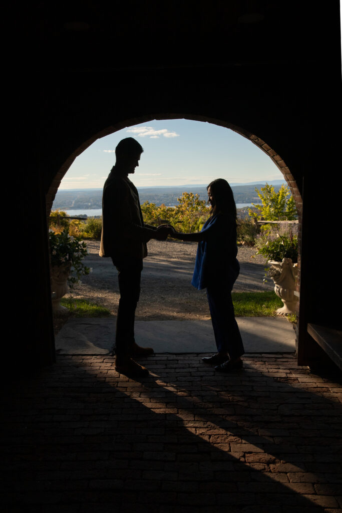 Couple elopes in Hudson Valley standing in archway silhouetted with expansive mountain view behind them